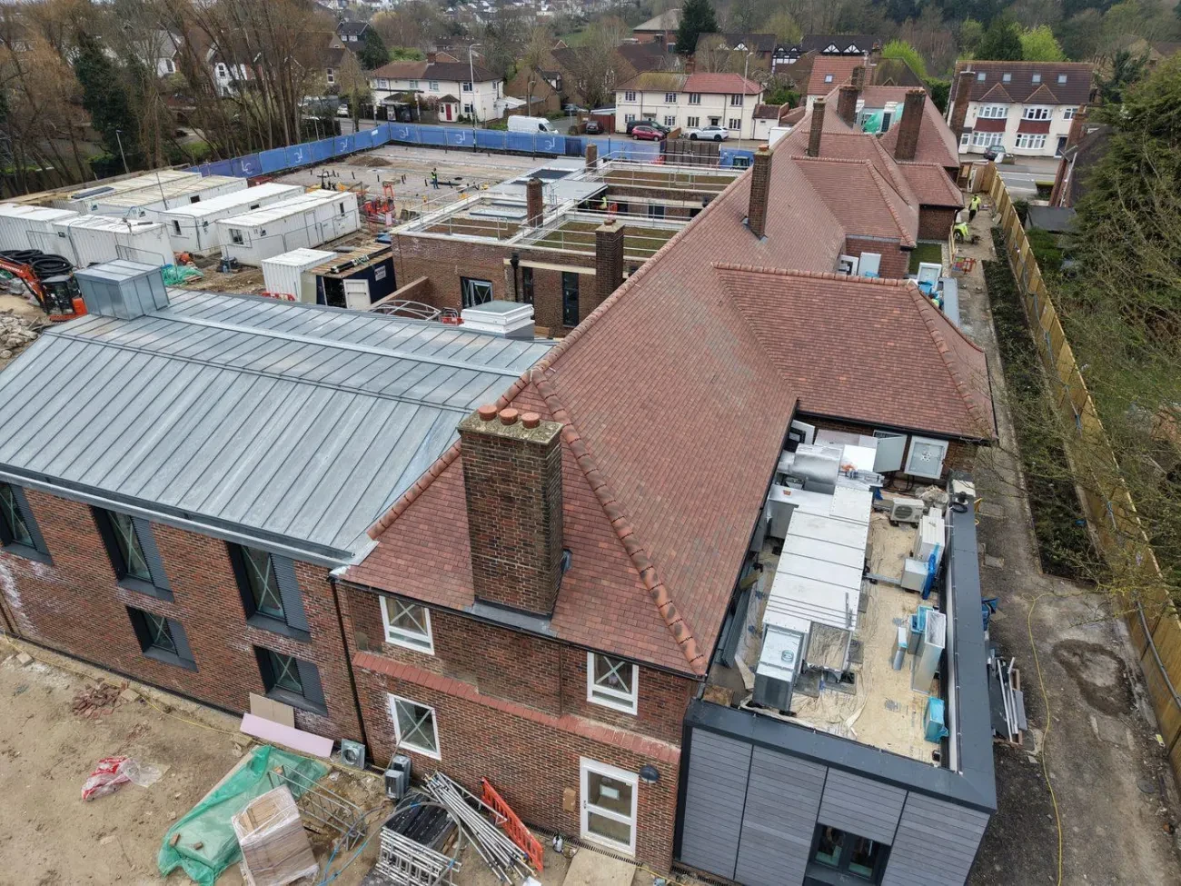 Wide aerial showing the full site extent including the zinc-clad link roof, new build flat roofs with green roof areas and the main building re-roof.