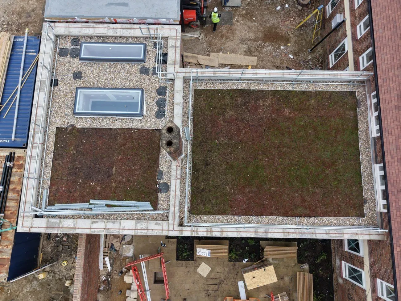 Overhead view of completed flat roof areas showing stone ballast perimeter zones, sedum green roof panels and rooflight installations.